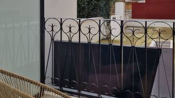 Un balcón con una silla de mimbre, una baranda de metal y vistas a un edificio con pared verde.