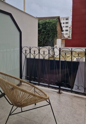 A balcony with a wicker chair, a metal fence, and a view of a building with a green wall. - Imi Hotel & Spa (Ourense)