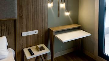 A hotel room with a bed, a small desk with a remote control, a wall-mounted light fixture, and a window.