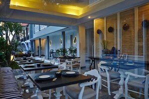 A modern restaurant with multiple tables and chairs, indoor plants, and a view of the outside. - The Kanjeng Suites Petitenget (Seminyak)