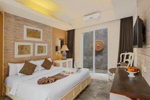 A hotel room with a bed, a desk, a chair, artwork on the wall, and a view through a glass door. - The Kanjeng Suites Petitenget (Seminyak)