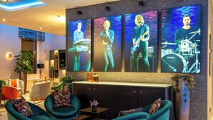 A modern lobby with teal armchairs, a reception desk, and wall-mounted screens displaying band performances. - Leonardo Royal Hotel Nurnberg (Nuremberg)