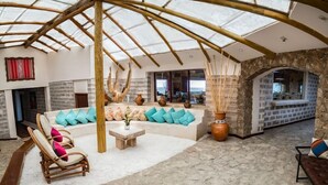 A spacious interior with a high ceiling, a stone wall, a wooden bench, a colorful striped rug, and a seating area with cushions. - Hotel De Sal Luna Salada (Uyuni)