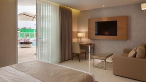 Ein Hotelzimmer mit Bett, Schreibtisch mit Stuhl, einer Couch, einem an der Wand befestigten Fernseher und einer Glastür zum Außenbereich.