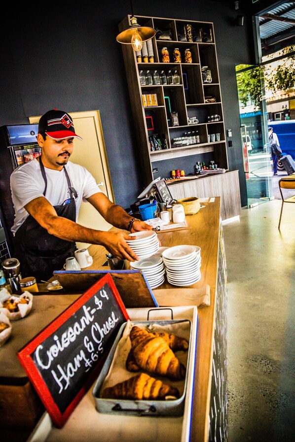 A bakery counter with a sign for Croissant Ham & Cheese, a tray of croissants, and a person stacking plates. - Veriu Central (Sydney)