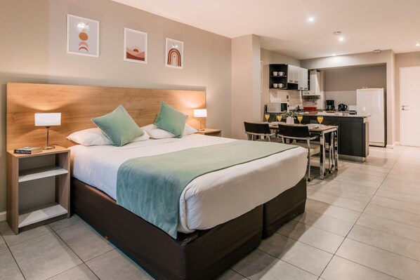 A modern hotel room with a large bed, bedside tables, a desk, and a kitchenette. - Departamentos La Vela (Ushuaia)