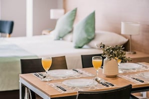 A neatly set dining table with two glasses of orange juice, a vase with greenery, and a bed with pillows in the background. - Departamentos La Vela (Ushuaia)