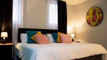 Quarto de hotel com cama, duas luminárias de cabeceira, um quadro grande na parede e janela com cortinas.