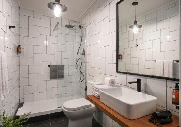 A modern bathroom with white tiled walls, a shower, a toilet, a sink, and a mirror. - The Pop Hotels (Santiago)
