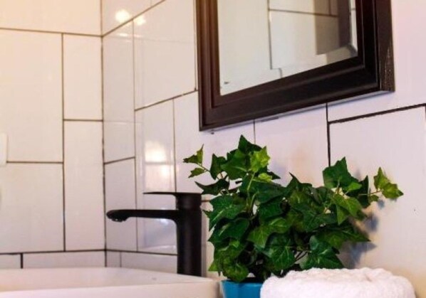Un baño con azulejos blancos, un grifo negro y una planta verde en una maceta azul.