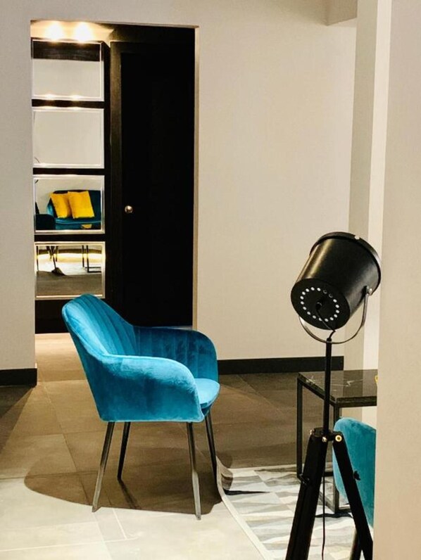 A room with a blue chair, a black floor lamp, and a door leading to a closet with shelves. - The Pop Hotels (Santiago)