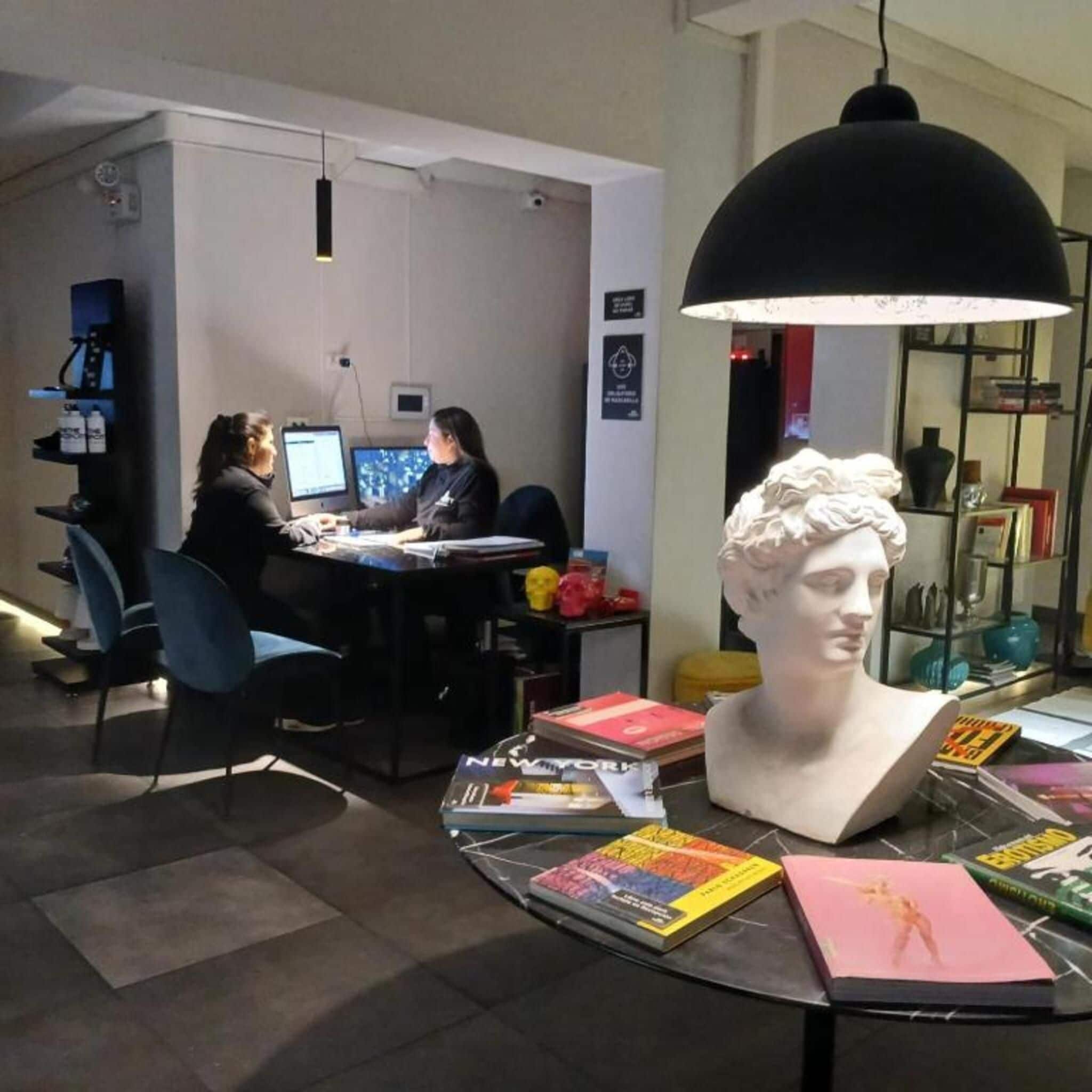 A modern office space with two people working at a desk, a bust sculpture on a table, and various books and items around.