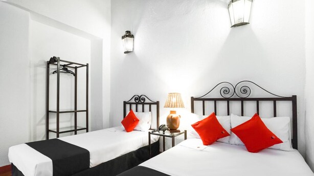 A hotel room with two beds, each with black and white bedding, red pillows, and a small bedside table with a lamp. - Capital O El Nito Posada (Oaxaca)
