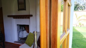 A cozy living room with a fireplace, a sofa, and a window overlooking a garden. - Casa Flor de Mayo (Tepoztlán)