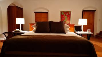 Habitación de hotel con una cama grande, dos mesitas de noche, un armario de madera y un cuadro colorido en la pared.
