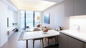 A modern living room with a large window, a dining area with a white table, and a kitchen with grey cabinets. - Lanson Place Mall of Asia (Pasay)