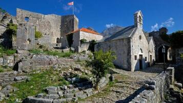 An ancient stone building with a bell tower, surrounded by ruins and a flag.