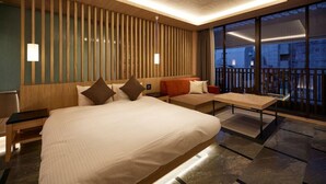 Ein modernes Hotelzimmer mit einem großen Bett, einer Couch, einem Esstisch und einem Balkon mit Geländer.