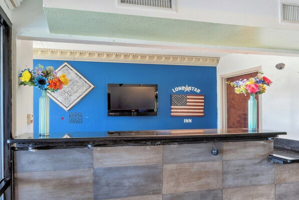 A reception desk with a television, a Lone Star Inn sign, and two vases with flowers. - Lonestar Inn Suites, Erick OK Hwy 40 (Erick)