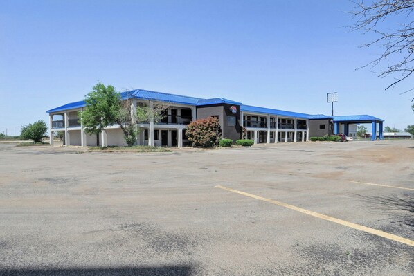 A two-story building with a blue roof, a parking lot, and a small garden area. - Lonestar Inn Suites, Erick OK Hwy 40 (Erick)