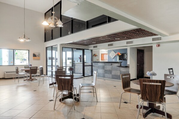 A spacious indoor area with multiple seating arrangements, including round tables and chairs, and a reception desk. - Lonestar Inn Suites, Erick OK Hwy 40 (Erick)