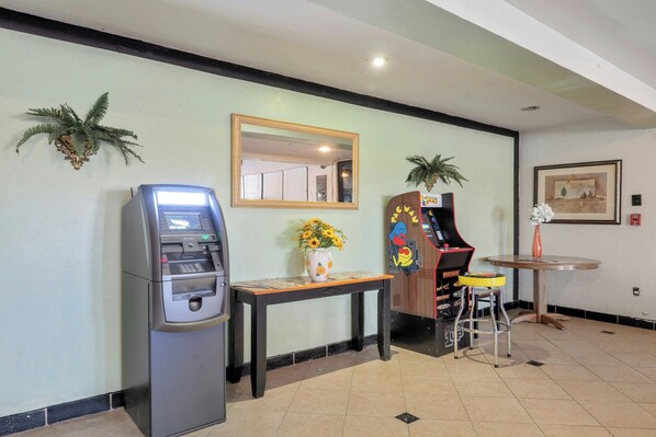 A room with a self-service kiosk, a mirror, a small table with a vase of flowers, and a small stool. - Lonestar Inn Suites, Erick OK Hwy 40 (Erick)