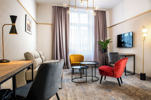 A modern hotel room with a sofa, two chairs, a small table, a TV, and a large window with curtains. - Mr67 Mayera Rapaporta (Kraków)