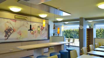 A modern restaurant interior with a long counter, blue and yellow seating, and large windows offering a view of greenery.