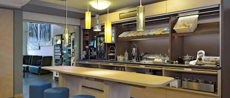 A modern kitchen with a long counter, hanging pendant lights, and a seating area with blue stools.