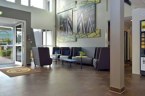 A hotel lobby with a reception desk, seating area, and artwork on the walls. - B&B Hotel Leipzig Nord (Leipzig)