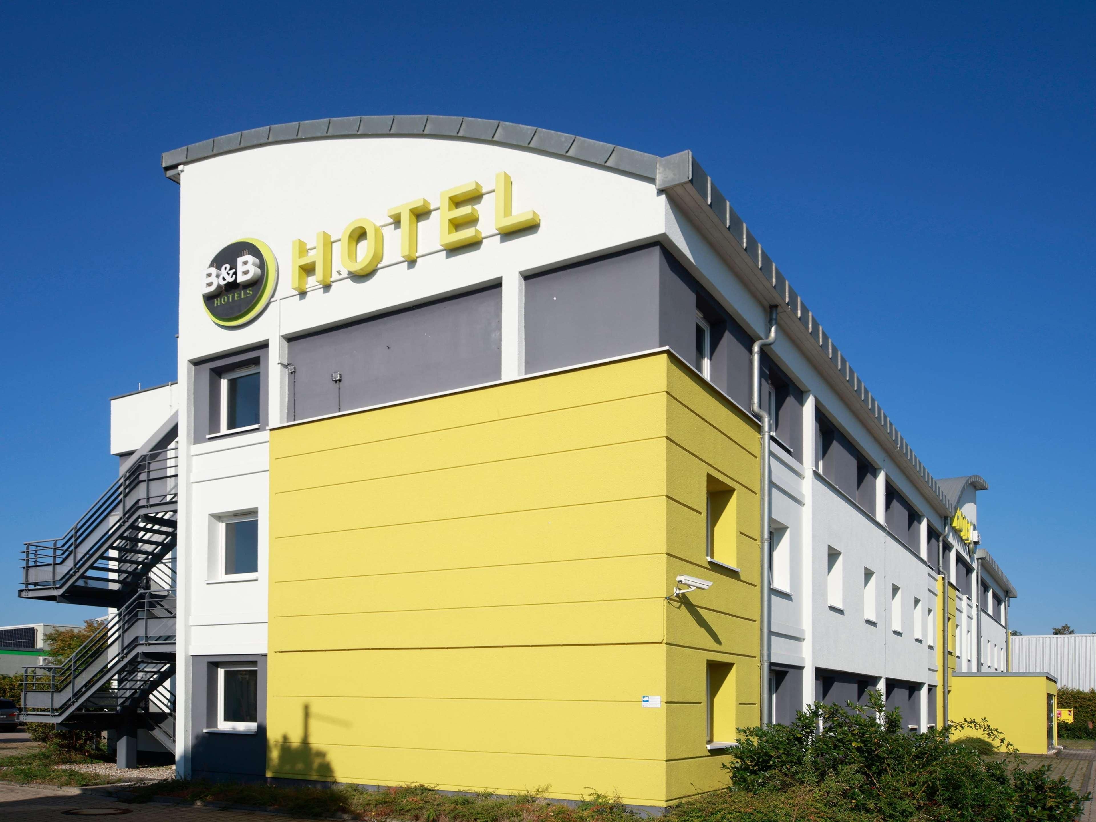 Um edifício de hotel moderno com fachada amarela e uma placa com a inscrição "B&B HOTELS".