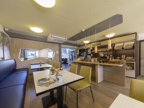 A modern dining area with a central table, chairs, and a counter with kitchen appliances. - B&B Hotel Leipzig Nord (Leipzig)