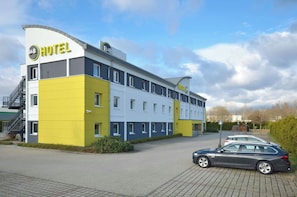 A hotel with a modern design, featuring a yellow and white color scheme, multiple windows, and a car parked in front. - B&B Hotel Leipzig Nord (Leipzig)