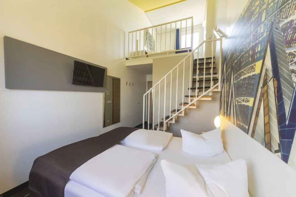 A hotel room with a bed, a staircase, and a mural on the wall.