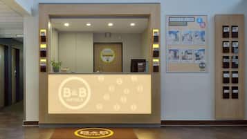 A reception desk with a B&B Hotels logo, a digital display, and a framed welcome sign.