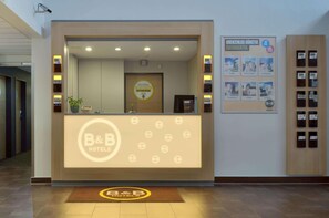 A reception desk with a B&B Hotels logo, a digital display, and a framed welcome sign. - B&B Hotel Leipzig Nord (Leipzig)