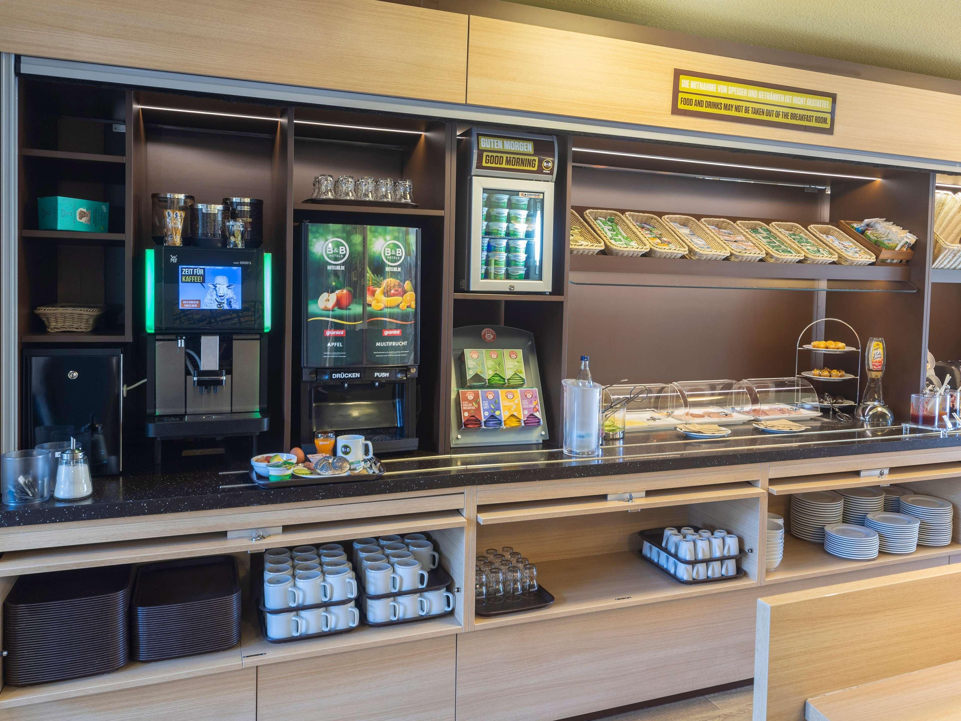 Um balcão de café da manhã com máquina de café, estação de chá e diversas opções de comida.