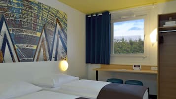 A hotel room with two beds, a desk, a mirror, and a window with a view of greenery.