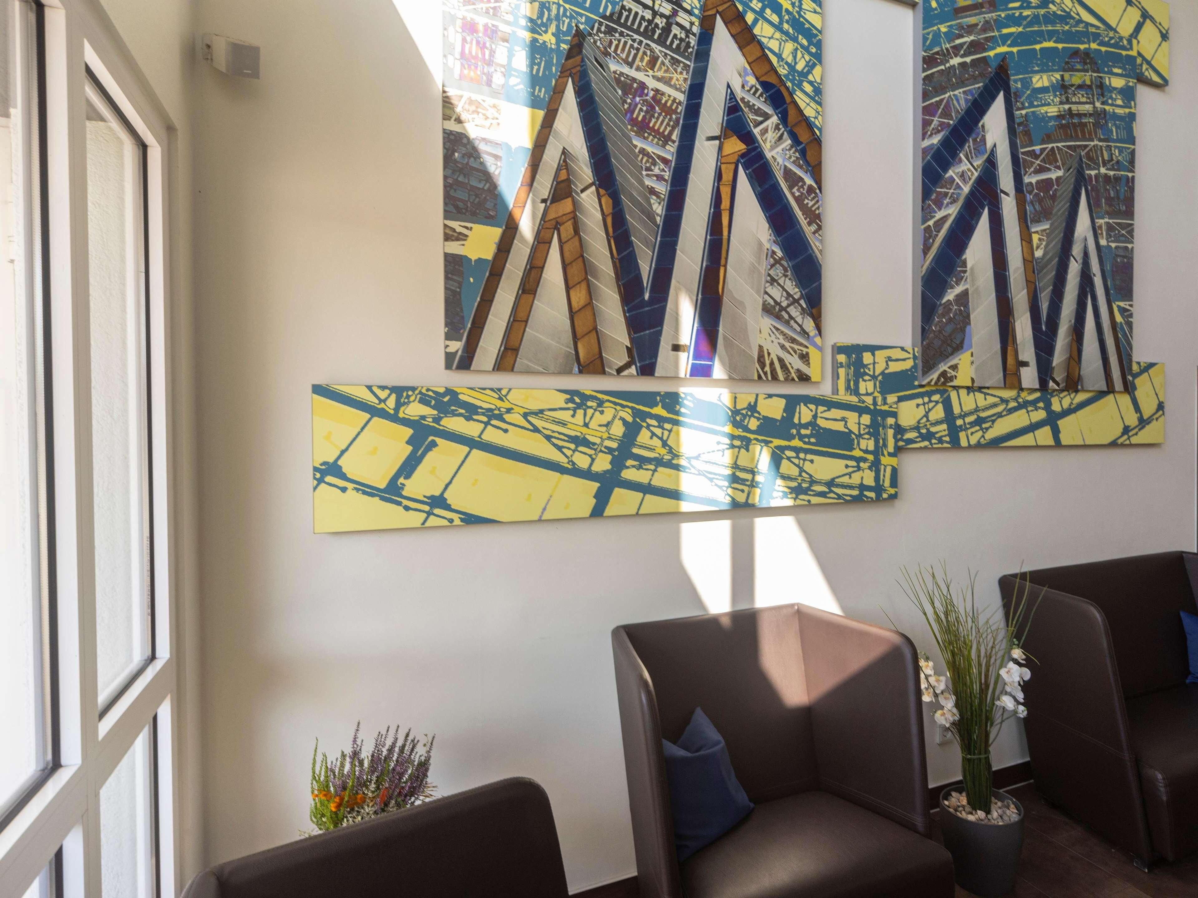 Um hall moderno com arte abstrata nas paredes, assentos confortáveis e uma grande janela que oferece luz natural.