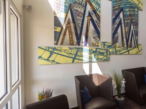 A modern lobby with abstract art on the walls, comfortable seating, and a large window providing natural light. - B&B Hotel Leipzig Nord (Leipzig)