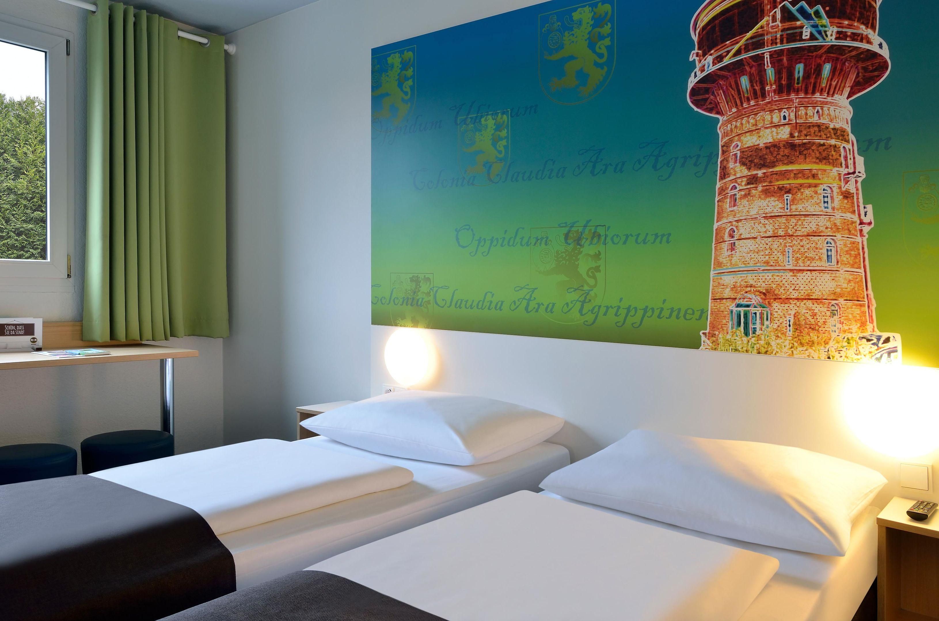 Habitación de hotel con dos camas, un escritorio y un mural grande de un faro.