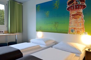 Quarto de hotel com duas camas, uma escrivaninha e um grande mural na parede com um farol.