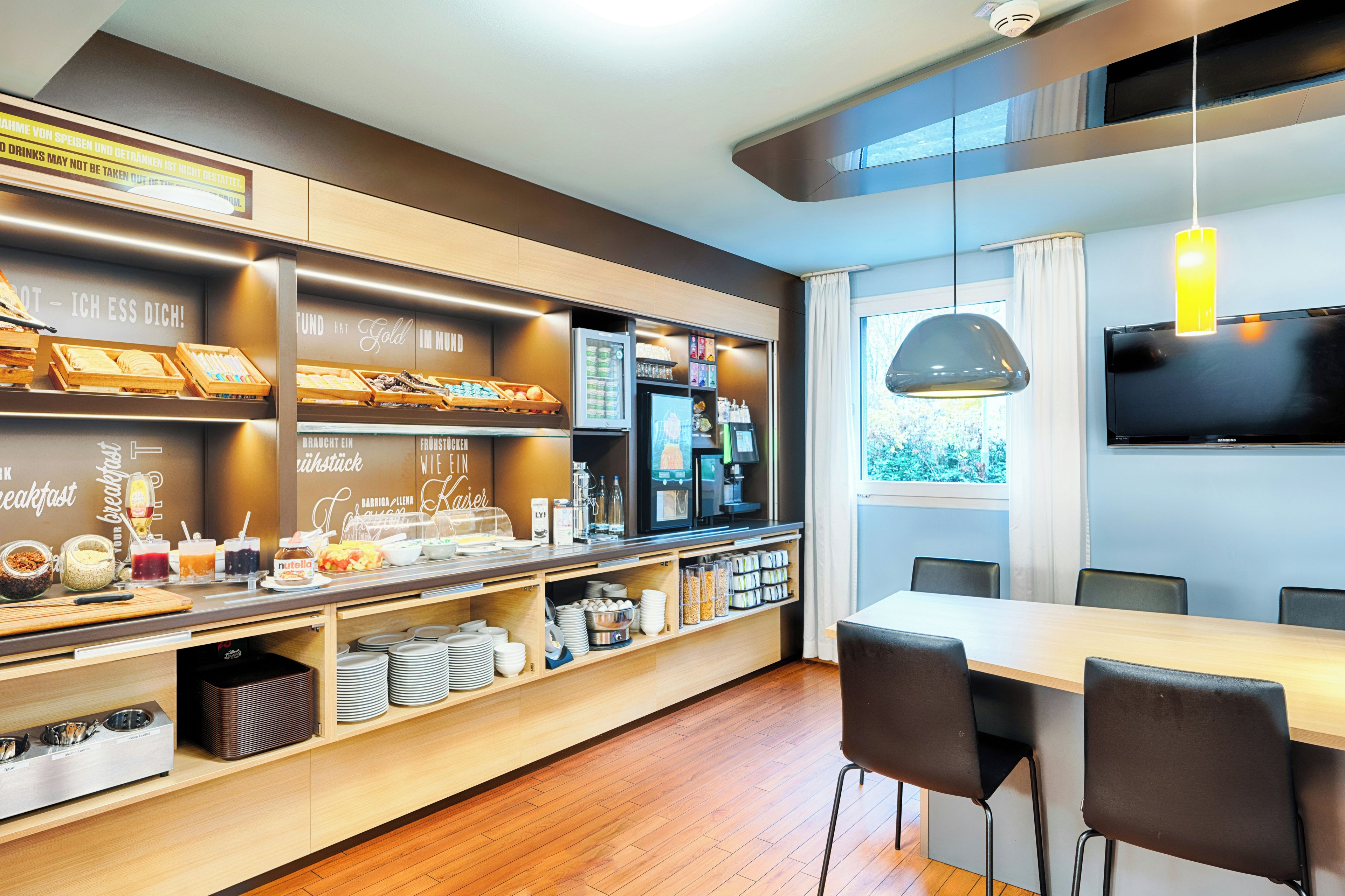 A modern breakfast bar with a variety of food options, a coffee station, and a seating area with a large window.