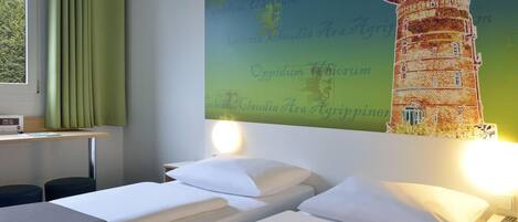 A hotel room with two beds, a desk with a lamp, a window with curtains, and a wall with a lighthouse mural.