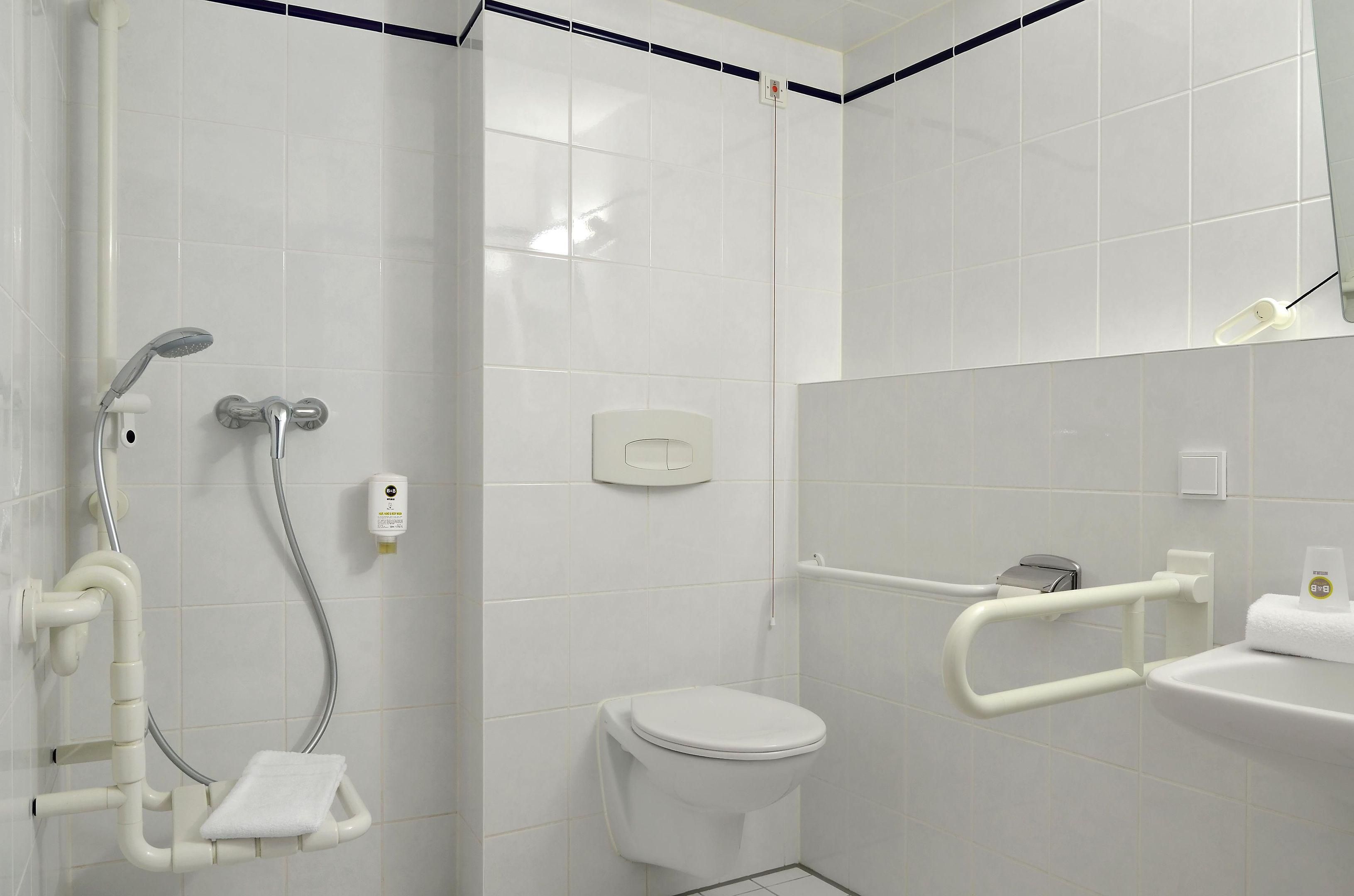 Ein Badezimmer mit Toilette, einer Duschkabine mit Haltegriffen und einem Waschbecken mit Handtuch.