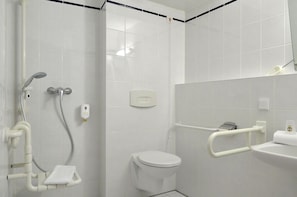 Uma casa de banho com sanita, chuveiro com barras de apoio e lavatório com toalha.