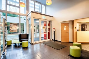 A modern hotel lobby with a reception desk, seating area, and glass doors leading outside. - B&B Hotel Köln-frechen (Frechen)