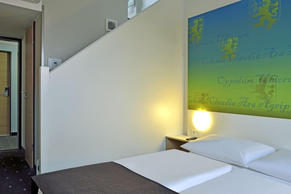 Quarto de hotel com cama, mesa de cabeceira, luminária na parede e escada.
