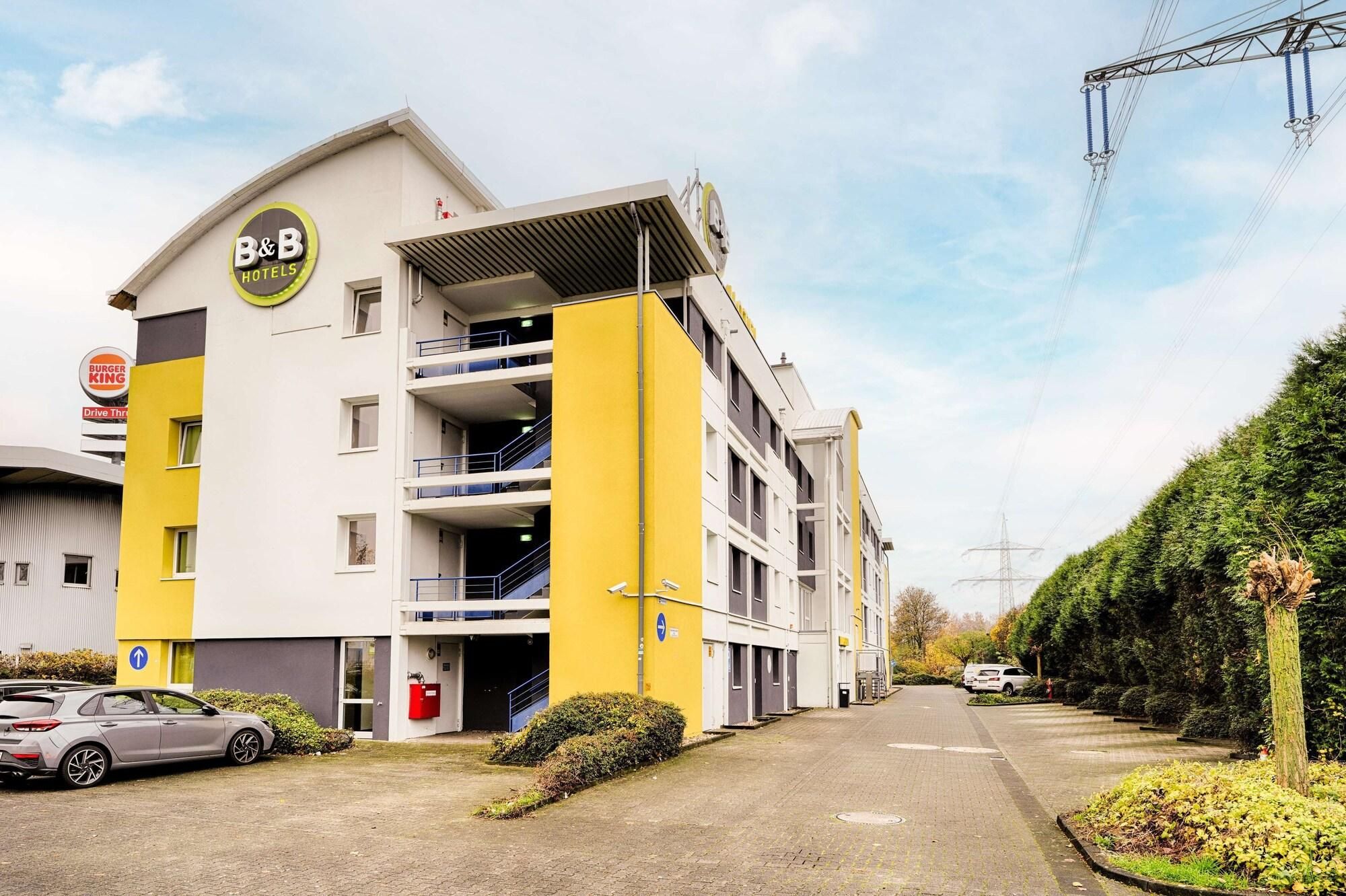 A B&B hotel with a yellow and white facade, multiple floors, and a parking area with a car.