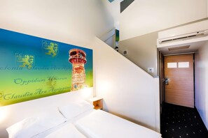 A hotel room with a bed, a wall-mounted artwork of a lighthouse, a wooden door, and an air conditioning unit. - B&B Hotel Köln-frechen (Frechen)